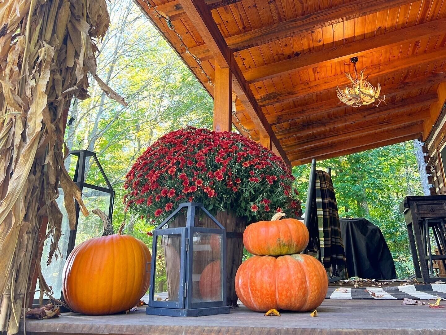 A wooden porch with a large lantern, a decorative flower arrangement, and pumpkins.