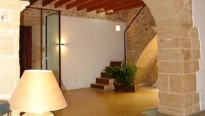 A spacious interior with a stone wall, a wooden ceiling, and a staircase leading to an upper level. - Casa Muralla, Charming Old Town House with Private Pool Alcudia (Alcudia)
