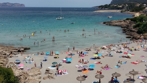 A beach with people sunbathing and swimming, umbrellas, and boats in the water. - Casa Muralla, Charming Old Town House with Private Pool Alcudia (Alcudia)