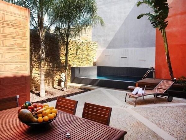Un patio con una mesa lista para comer, una piscina y un área de estar con una silla y una pequeña mesa.