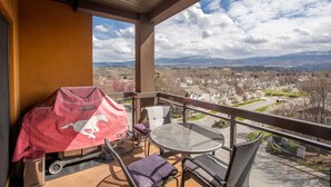 A balcony with a barbecue grill, wicker chairs, and a table. - Mountainview getaway at Playa Del Sol (Kelowna)