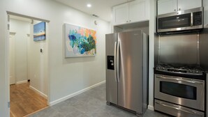Una cocina moderna con electrodomésticos de acero inoxidable, piso de baldosas grises y un pasillo con piso de madera que lleva a una puerta.