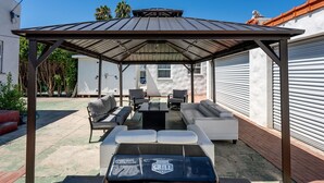 Un patio techado al aire libre con una parrilla, zona de estar y vista al jardín.