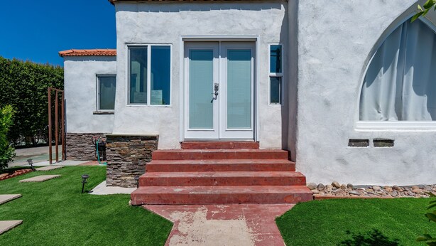 Una casa de dos pisos con fachada blanca, techo de tejas rojas y entrada principal con puertas dobles.