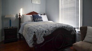 Une chambre à coucher avec un lit en bois, une table de chevet, une lampe et une fenêtre avec des stores.