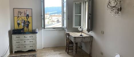 A bedroom with a bed, a desk, a chair, a dresser, a window with a view, and a chandelier.