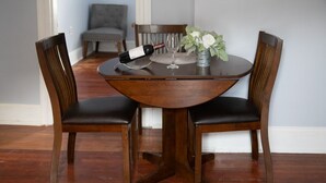 A round wooden dining table with two chairs, a wine bottle, and a glass on it.