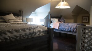 A bedroom with two beds, a sloped ceiling, and a hanging light fixture.