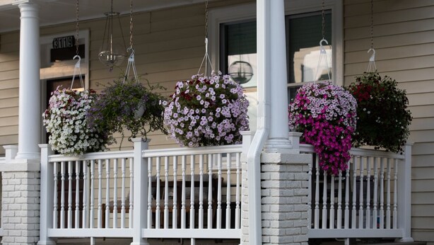 A porch with white railings and hanging flower baskets.