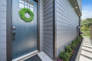 A modern house with a grey door, a no smoking sign, and a small porch with plants.
