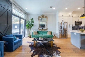 Moderni olohuone, jossa on sohva, sohvapöytä sekä keittiöalue, jossa on kaappeja ja kodinkoneita.