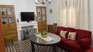 Een woonkamer met een rode bank, een glazen salontafel, een televisie en een open haard.