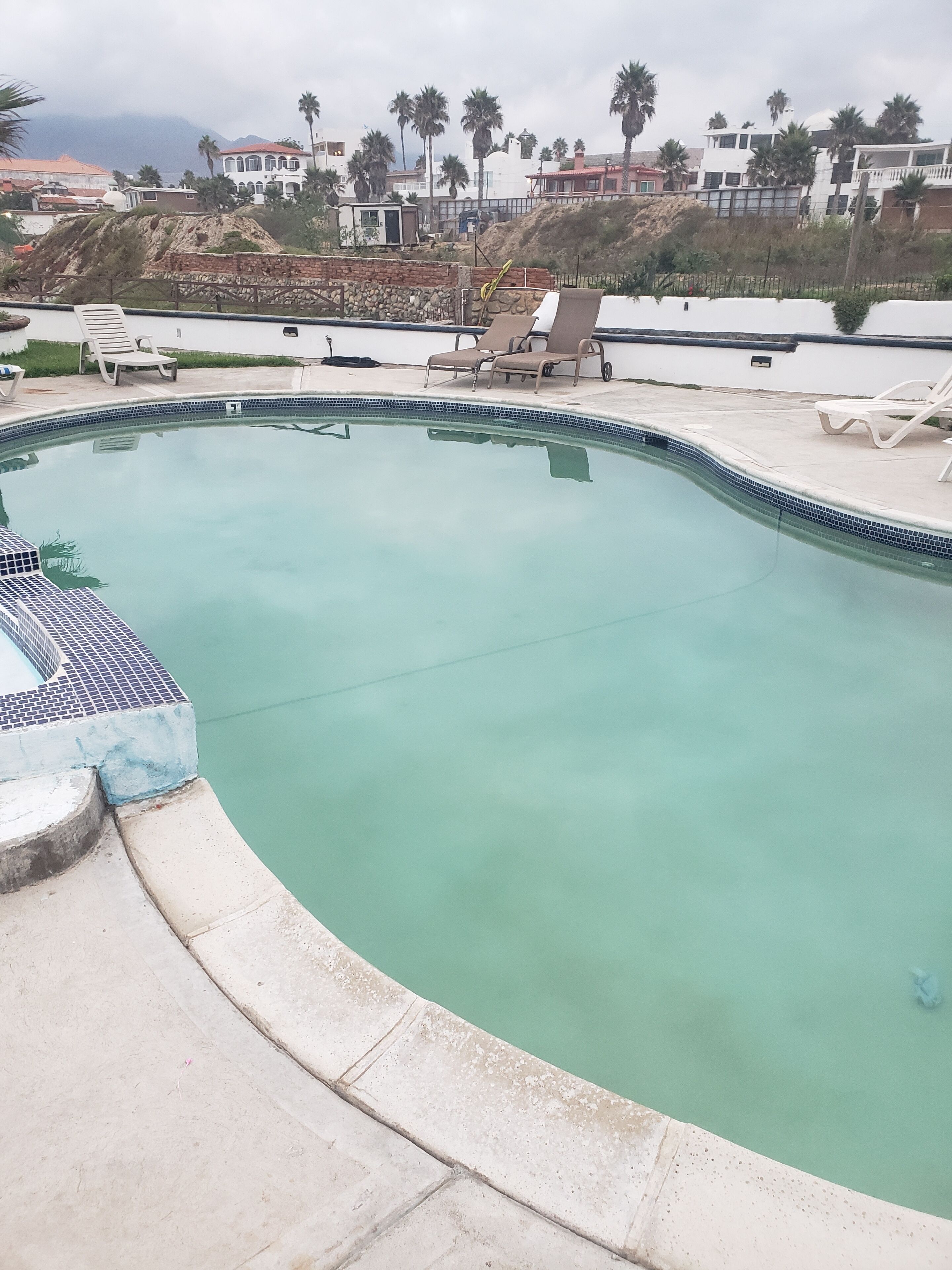 A swimming pool with a tiled edge, surrounded by lounge chairs and a stone wall.