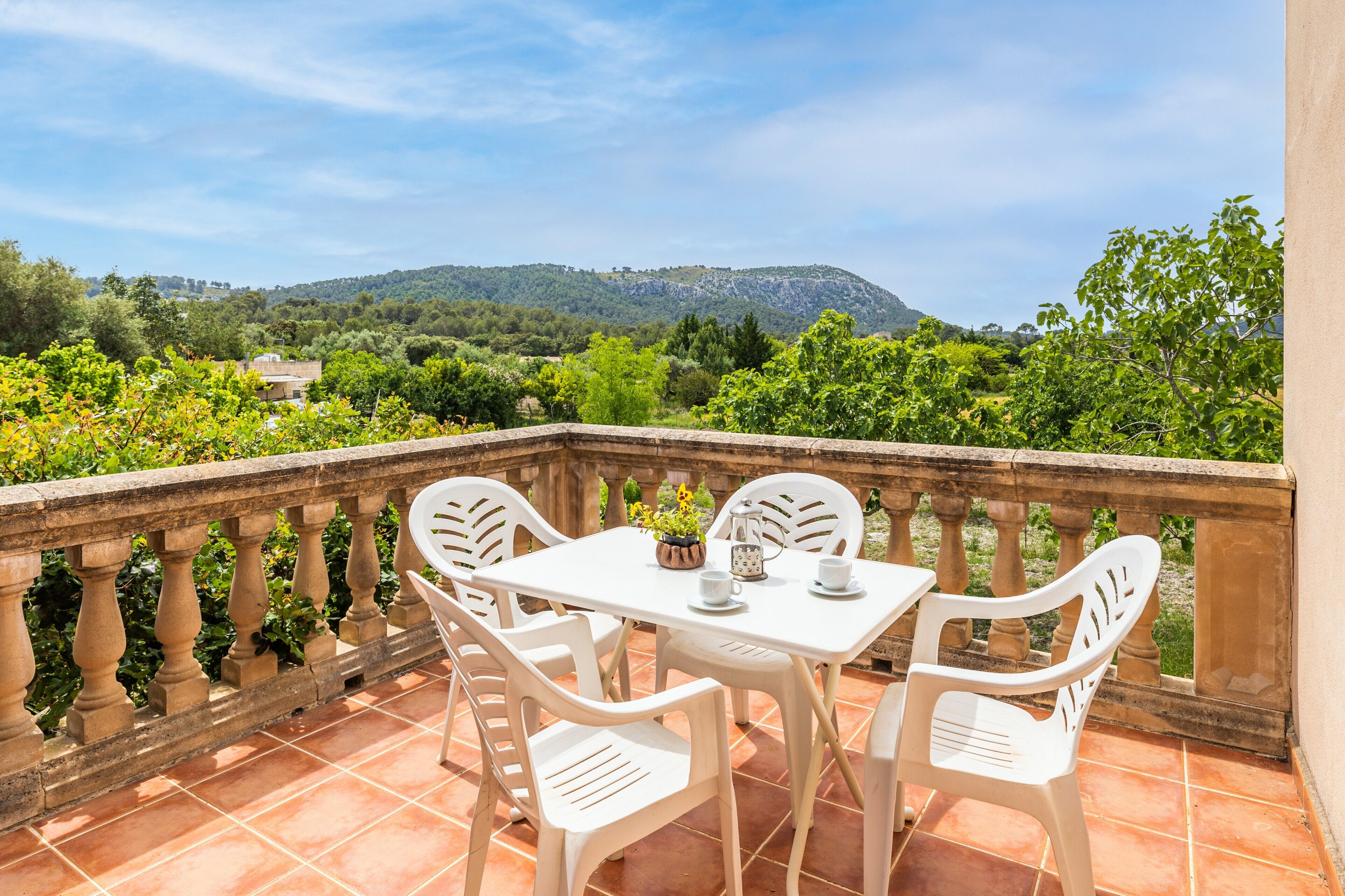 Eine Terrasse mit Tisch und Stühlen, Blick auf Grünflächen und Hügel, sowie eine Steinbalustrade.