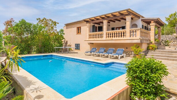 Vista a la piscina de una casa de dos pisos con balcón, piscina y sillas de descanso.