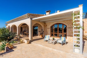 Una casa con patio, mobiliario exterior y una pérgola.
