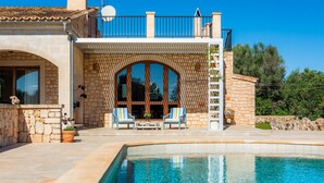 Ein Poolbereich mit Steinmauer, zwei Liegestühlen und einer überdachten Sitzgruppe mit Blick auf den Pool.