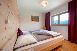 Une chambre avec une tête de lit en bois, un lit avec des oreillers, un tableau au mur, une fenêtre avec des rideaux et un luminaire au plafond.