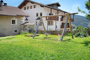 Une maison avec une balançoire dans le jardin, une clôture en bois et une montagne en arrière-plan.