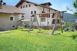 A house with a swing set in the yard, a wooden fence, and a mountain in the background.