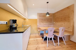 A modern kitchen with a coffee maker, wooden wall paneling, and a dining area with chairs.