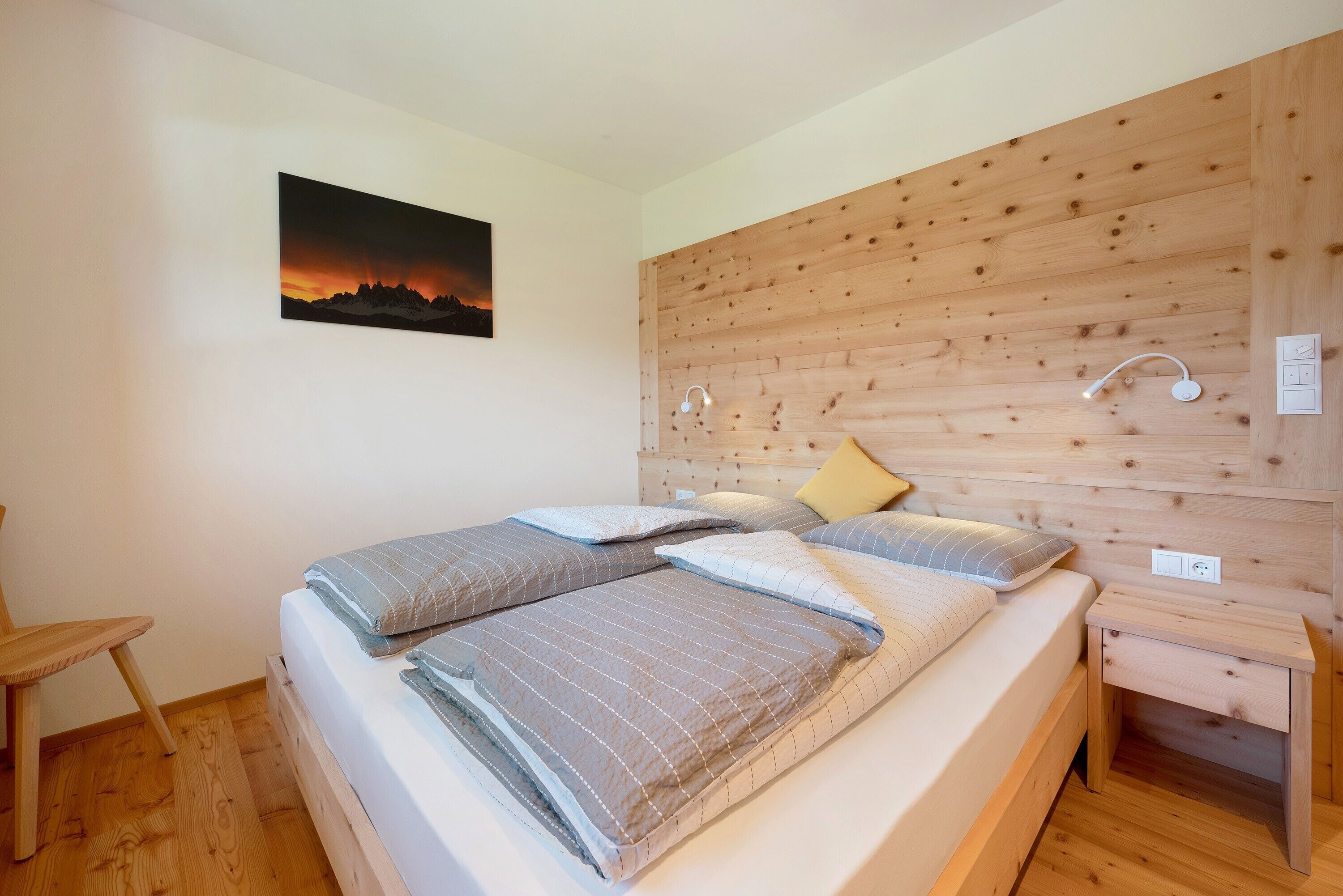 Ein Schlafzimmer mit einem hölzernen Kopfteil, einem Bett mit vielen Kissen, einem Nachttisch und einer Wandleuchte.