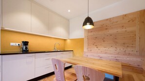 Una cocina moderna con una mesa de comedor de madera, dos sillas, una cafetera y una lámpara colgante.