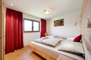 A bedroom with a wooden bed, red curtains, a window, a headboard, and a wall-mounted lamp. - Vacation Apartment "Teutenhofer Kirsche" on the Farm with Mountain View & Garden (Feldthurns)