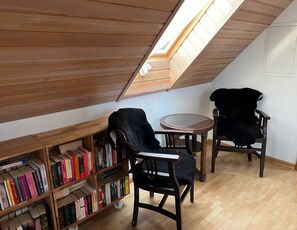 A cozy attic room with wooden bookshelves, two dark chairs, and a small round table.