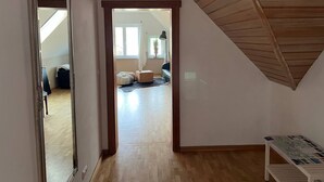 A spacious loft bedroom with a sloped ceiling, wooden flooring, and a large mirror.