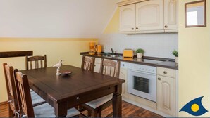 A dining area with a wooden table and chairs, a kitchen with white cabinets and a clock on the wall. - Vacation apartment at Krebssee Whg Adler - Adler (Heringsdorf)