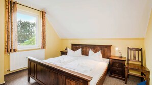 A bedroom with a wooden bed, a nightstand, a chair, and a window with curtains. - Vacation apartment at Krebssee Whg Adler - Adler (Heringsdorf)
