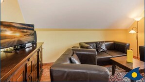 A living room with a leather sofa, a coffee table, a flat-screen TV on a wooden cabinet, and a floor lamp. - Vacation apartment at Krebssee Whg Adler - Adler (Heringsdorf)