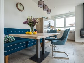 A modern kitchen with a dining area, featuring a blue sofa, a wooden table, and a vase with flowers.