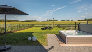 Ett bubbelbad med en gräsyta och solstolar, en inhägnad åker och en klar himmel.