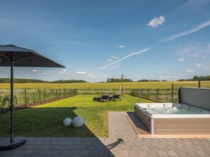 Una vasca idromassaggio con area verde e poltrona prendisole, un campo recintato e un cielo sereno.
