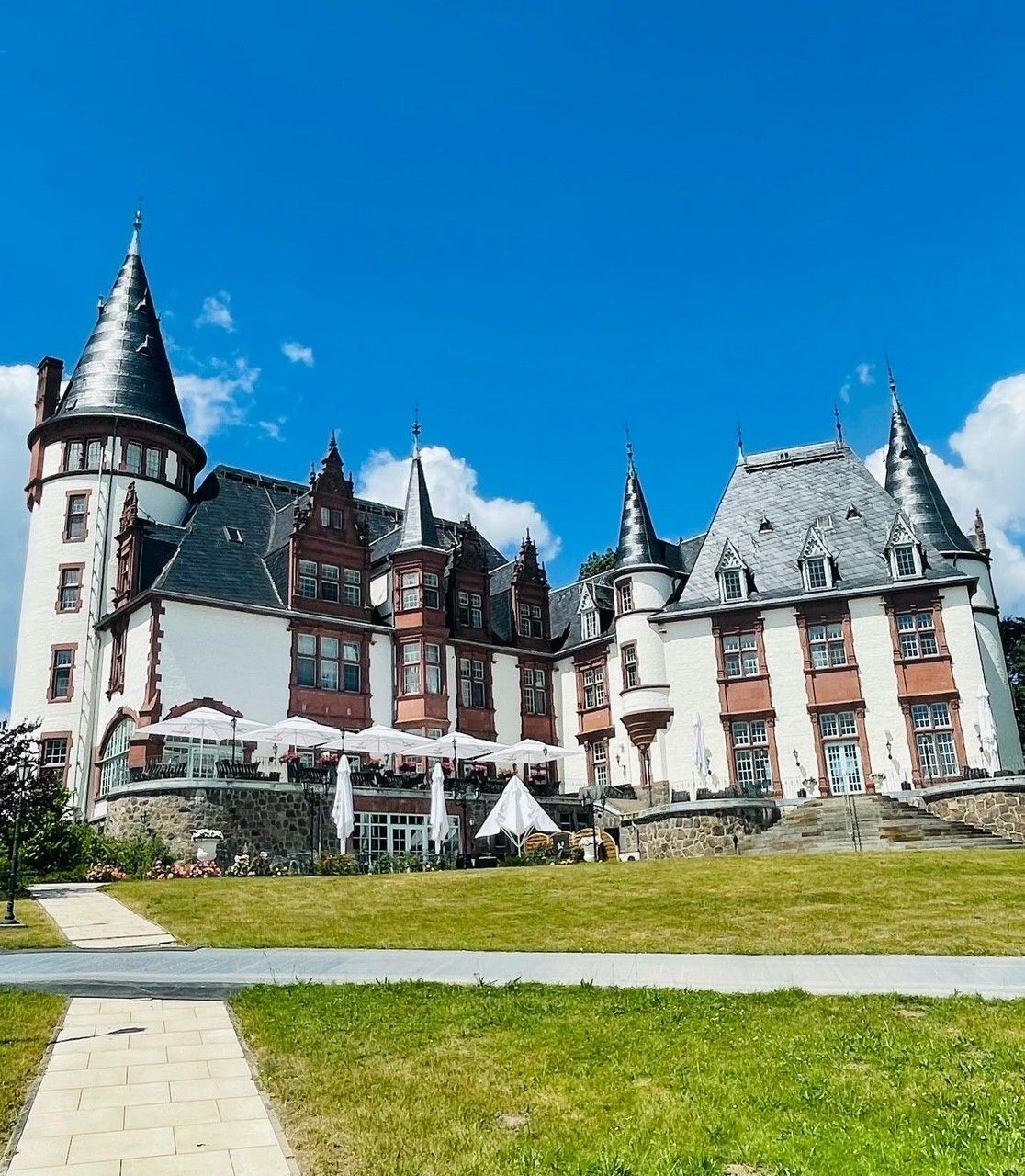 A large, historic building with multiple towers and a well-maintained lawn in front.