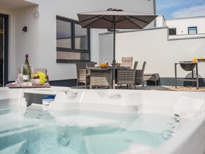 A hot tub with a table and chairs, an umbrella, and a grill outside a building.