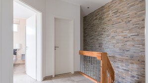 En modern hall med en trätrappa, en vit dörr och en vägg med en strukturerad stenbeklädnad.