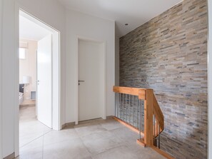 Un corridoio moderno con una scala in legno, una porta bianca e un muro di pietra strutturato.