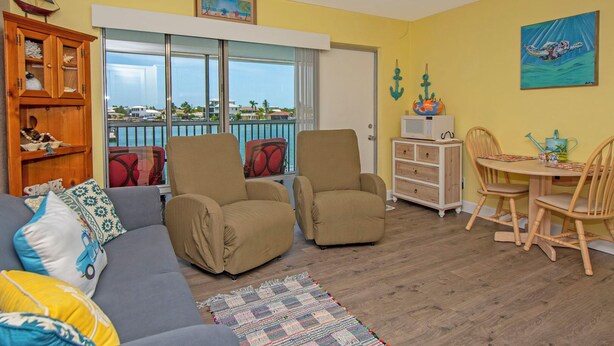 A cozy living room with a sofa, two armchairs, a wooden cabinet, and a dining area with a table and chairs.