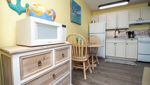 A compact kitchen with white cabinets, a microwave, a stove, and wooden chairs at a small table.