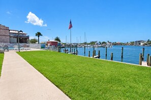 Un puerto deportivo con barcos amarrados, una zona verde, un sendero y un edificio con una bandera.