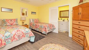A bedroom with two beds, a wooden dresser, a ceiling fan, and a bathroom with a sink and mirror.