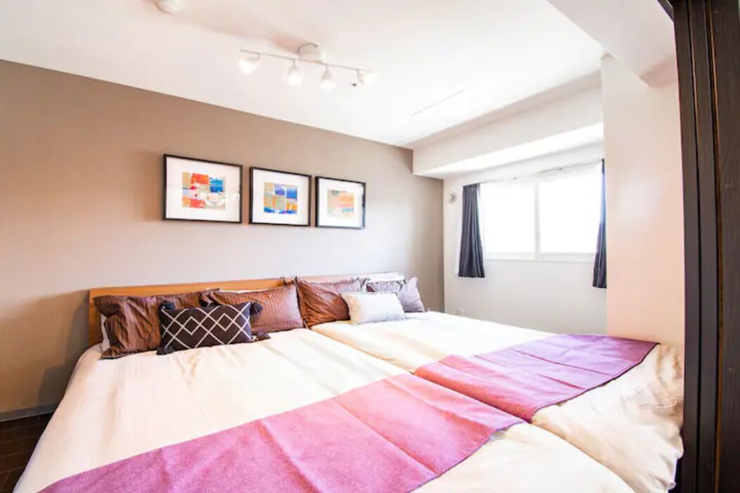 Une chambre d’hôtel avec un grand lit, une fenêtre avec des rideaux et deux tableaux encadrés accrochés au mur.