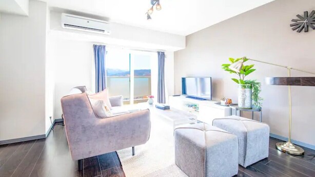 Een moderne woonkamer met een bank, voetenbankje, televisie en een plant.