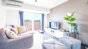 Een moderne woonkamer met een bank, fauteuils, een salontafel, een televisie en een kamerplant.