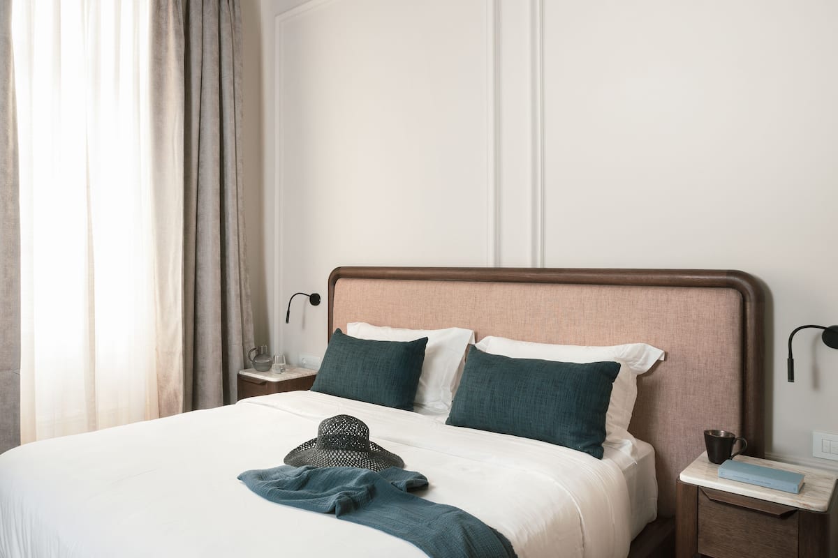 A neatly made bed with pillows, a bedside table with a lamp, and a window with curtains.