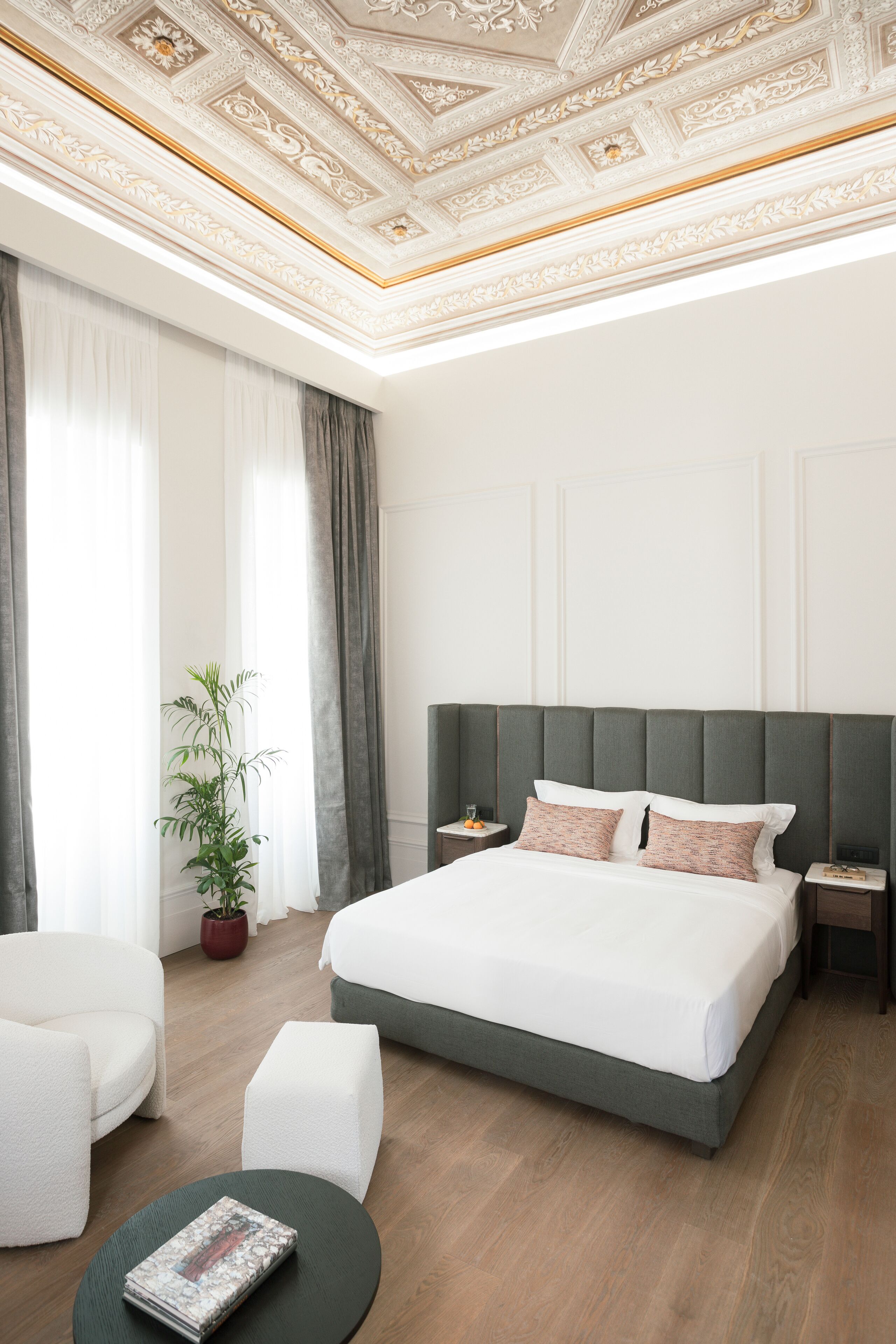 A hotel room with a large bed, two bedside tables, a potted plant, a chair, and a round table.