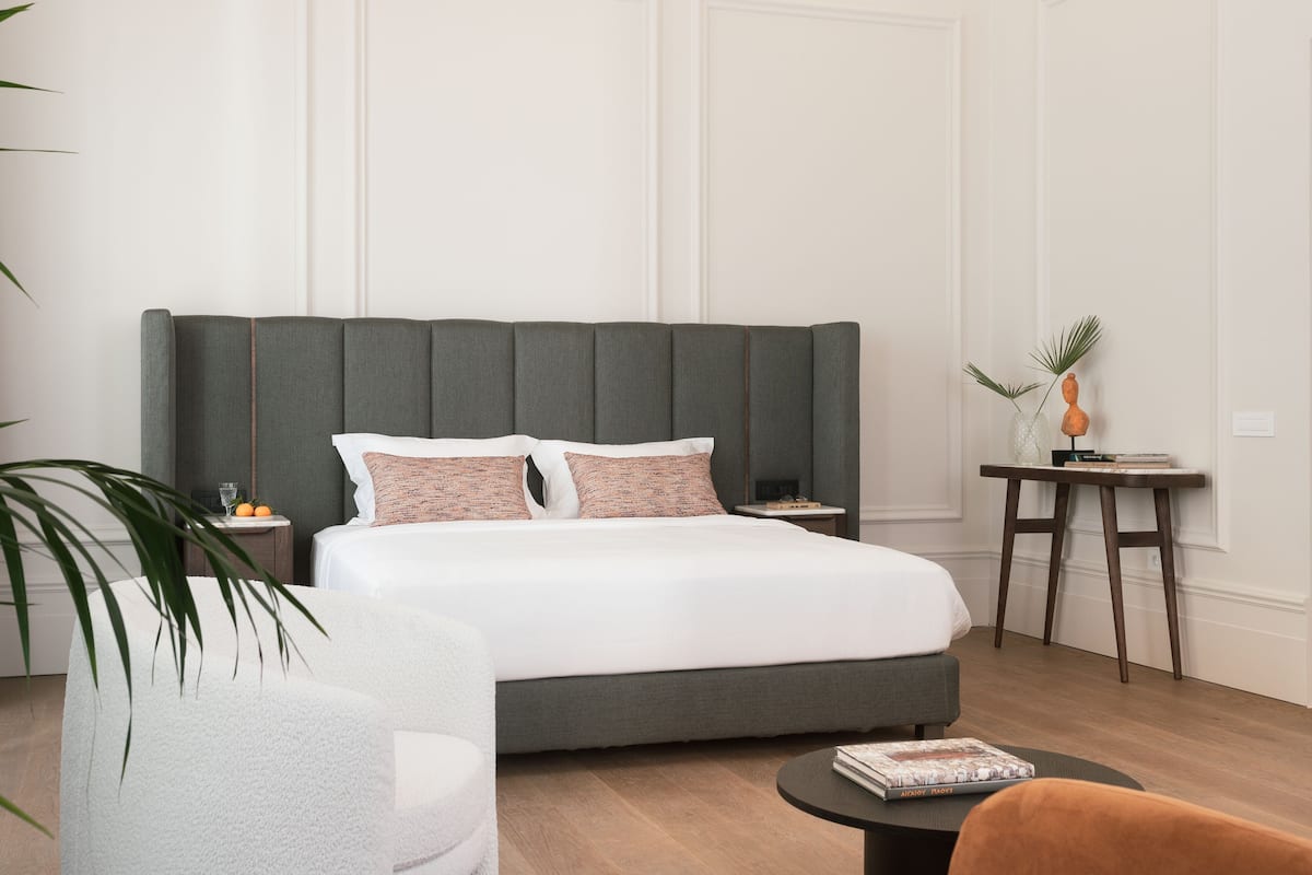 A modern bedroom with a large bed, bedside tables, a small side table, a chair, and a coffee table.